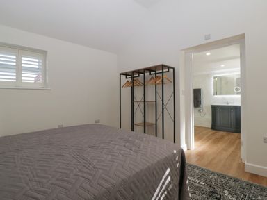 A bedroom with a bed, open wardrobe with hangers, and an open door leading to a bathroom at Singletree Cottage in Swainsford near Mere
