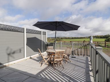 An outdoor patio with a round wooden table and four chairs under a large umbrella at Singletree Cottage in Swainsford near Mere