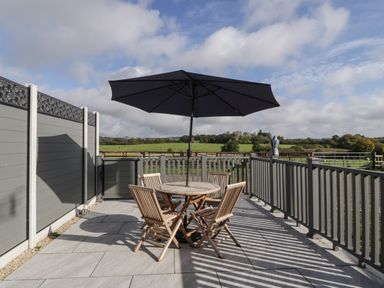 A patio with a round table umbrella and four wooden chairs overlooking a green field at Singletree Cottage in Swainsford near Mere