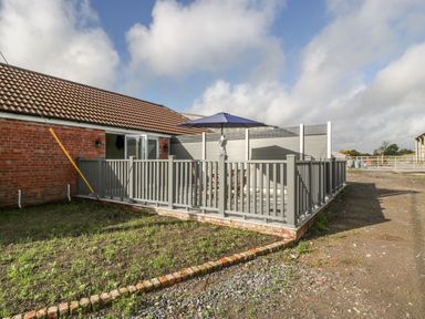 An outdoor patio area with a gray fence table with umbrella near a brick building at Singletree Cottage in Swainsford near Mere