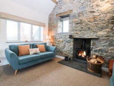A living room with a sofa, fireplace, and windows at Yr Hen Felin in Dyffryn Ardudwy