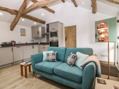 A kitchen and sitting area with exposed wooden beams a teal sofa and modern kitchen units at Y Stabl in Dyffryn Ardudwy