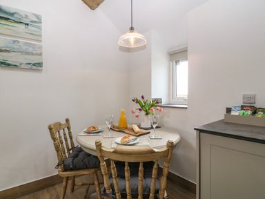 A dining area with a round table set with croissants orange juice and flowers two wooden chairs and paintings on the wall at Y Stabl in Dyffryn Ardudwy