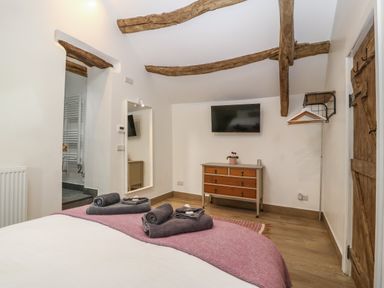 A bedroom with wooden beams a dresser a wall-mounted tv and towels on a bed at Y Stabl in Dyffryn Ardudwy