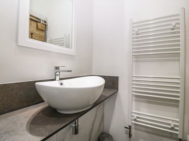 A bathroom with a white vessel sink on a stone countertop a mirror and a white towel radiator at Y Stabl in Dyffryn Ardudwy