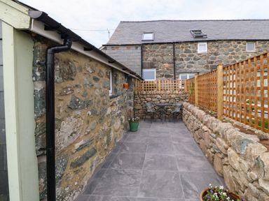 An outdoor patio area with stone walls two chairs and a table at Y Stabl in Dyffryn Ardudwy