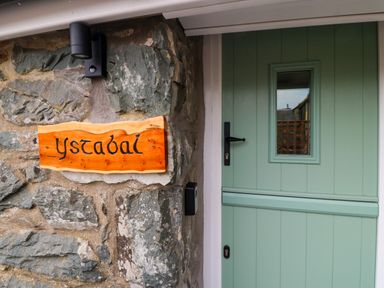 A green door with a window and a wooden sign reading ystabal on a stone wall at Y Stabl in Dyffryn Ardudwy