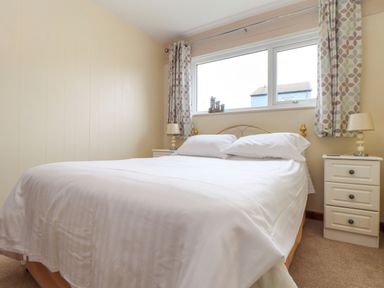 A bedroom with a double bed white bedding two bedside tables lamps and a window with patterned curtains at Skylarks Trevellas Nr St Agnes