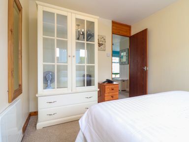 A bedroom with a white wardrobe glass doors wooden bedside table with a hairdryer and an open door at Skylarks Trevellas Nr St Agnes