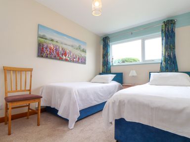 A bedroom with two single beds a wooden chair a window with curtains and a floral painting on the wall at Skylarks Trevellas Nr St Agnes