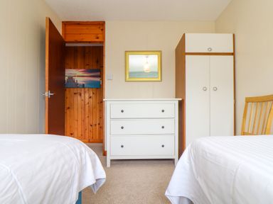A bedroom with two beds a white dresser a wardrobe a wooden chair and an open door showing a hallway at Skylarks Trevellas Nr St Agnes