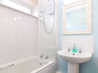 A bathroom with a bathtub shower combination a white sink with hand soap and a mirror at Skylarks Trevellas Nr St Agnes