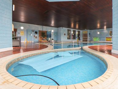 An indoor swimming pool area with a small shallow pool and a larger pool in a room with blue walls and a dark wooden ceiling at Skylarks Trevellas Nr St Agnes