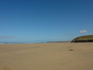 A sandy beach with a few people near the water and hills in the background at Skylarks Trevellas Nr St Agnes