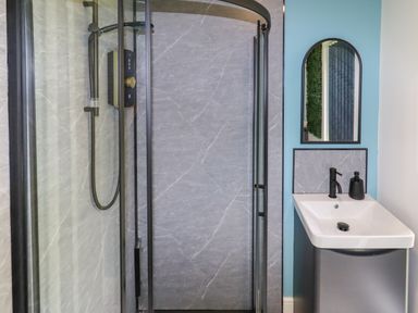 A bathroom with a curved glass shower enclosure and a sink with a mirror above at Valley Lodge 4 - North Wales Eco Lodges in Graigfechan near Ruthin