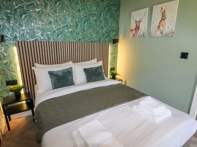 A bed with green pillows and blanket two side tables with plants and animal paintings on the wall at Valley Lodge 4 - North Wales Eco Lodges in Graigfechan near Ruthin