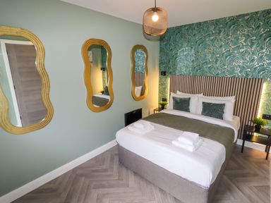A bedroom with a double bed two pillows and folded towels three wavy mirrors on a wall and patterned wallpaper behind the bed at Valley Lodge 4 - North Wales Eco Lodges in Graigfechan near Ruthin