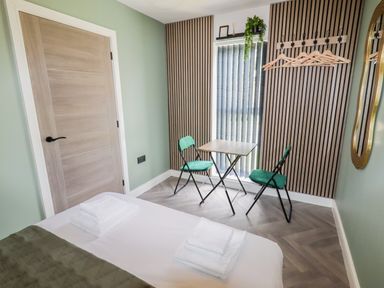 A bedroom with a bed, two chairs, small table, hanging hooks with hangers, and a door at Valley Lodge 4 - North Wales Eco Lodges in Graigfechan near Ruthin