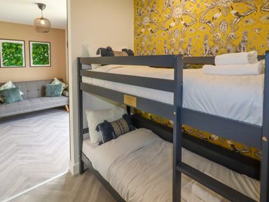 A bedroom with bunk beds next to a living room with a gray sofa and green cushions at Valley Lodge 4 - North Wales Eco Lodges in Graigfechan near Ruthin