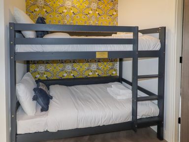 A bunk bed with white bedding and dark blue pillows in a room with yellow patterned wallpaper at Valley Lodge 4 - North Wales Eco Lodges in Graigfechan near Ruthin