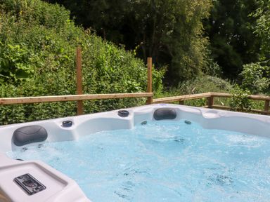 An outdoor hot tub with water jets and headrests on a wooden deck surrounded by greenery at Valley Lodge 4 - North Wales Eco Lodges in Graigfechan near Ruthin