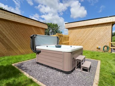 An outdoor hot tub with steps on gravel surrounded by grass and wooden fence at Valley Lodge 4 - North Wales Eco Lodges in Graigfechan near Ruthin