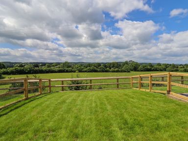 A grassy fenced yard with wooden rails and countryside view at Valley Lodge 4 - North Wales Eco Lodges in Graigfechan near Ruthin