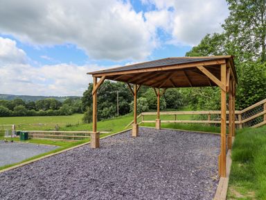 A wooden gazebo on a slate stone ground with a fenced green field in the background at Valley Lodge 4 - North Wales Eco Lodges Graigfechan near Ruthin