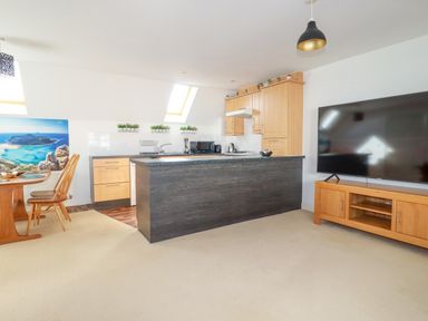A kitchen and dining area with wooden cabinets a dining table and chairs and a large flat screen tv at 20 Keay Heights in St Austell