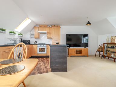 A kitchen and living area with wooden cabinets a dining table television and display cabinet at 20 Keay Heights in St Austell