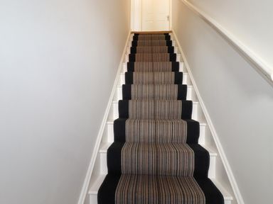 A staircase with white walls and a striped carpet runner at 20 Keay Heights in St Austell