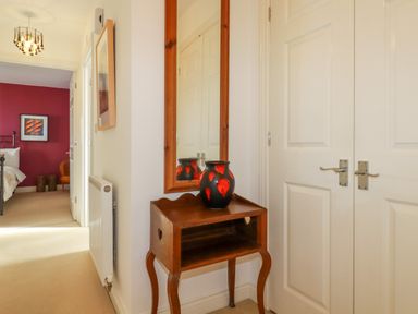 A hallway with a wooden table and mirror next to white doors and a view of a bedroom at 20 Keay Heights in St Austell