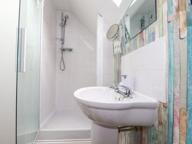 A bathroom with a wall-mounted sink a shower area with a glass door and colorful wooden panel walls at 20 Keay Heights in St Austell
