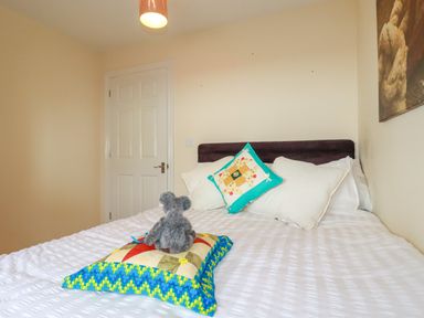 A bedroom with a made bed featuring white bedding two pillows a colorful cushion and a gray teddy bear at 20 Keay Heights in St Austell
