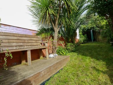 A garden with a wooden bench on a deck next to a wall with plants at 20 Keay Heights in St Austell