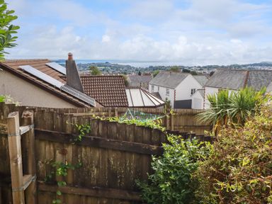 A view over rooftops with solar panels and a wooden fence with plants and a distant landscape at 20 Keay Heights in St Austell