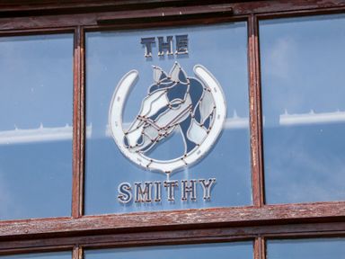 A stained glass window with a horse head and horseshoe design and the words the smithy at The Old Smithy in Lynton