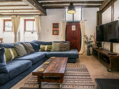 A living room with a blue sectional sofa a wooden coffee table a flat screen tv and a striped rug at The Old Smithy in Lynton