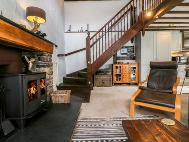 A living room with a wood burning stove wooden stairs and a black chair at The Old Smithy in Lynton