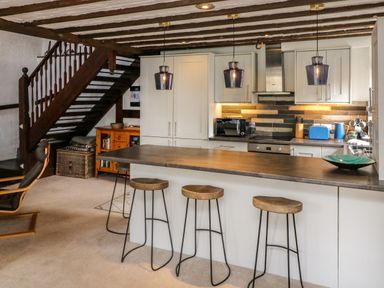 A kitchen with a wooden countertop island and four stools under exposed wooden beams at The Old Smithy in Lynton