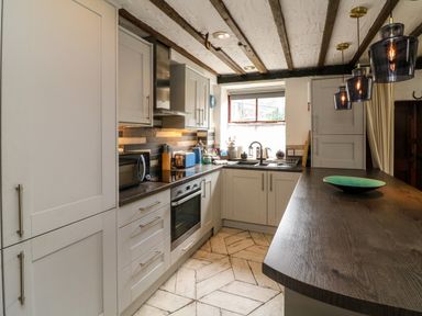 A kitchen with gray cabinets wooden countertop and hanging lights at The Old Smithy in Lynton