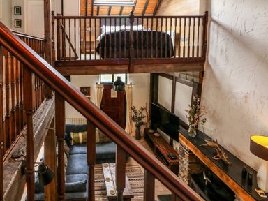 A living room with a blue sectional sofa a wooden coffee table a large tv and a loft bedroom above at The Old Smithy in Lynton