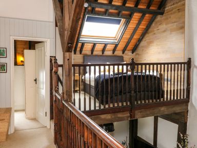 A loft bedroom with a bed under a skylight and wooden railing at The Old Smithy in Lynton