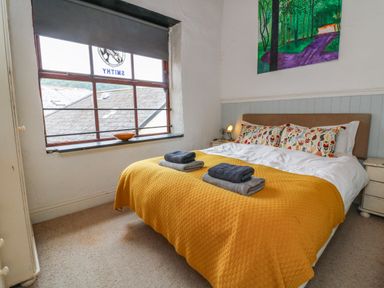 A bedroom with a double bed covered with a yellow blanket and folded towels on top at The Old Smithy in Lynton