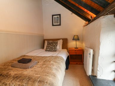 A small bedroom with a single bed a nightstand with lamp and a framed picture on the wall at The Old Smithy in Lynton