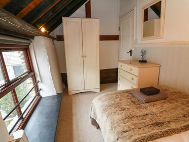 A bedroom with a bed covered with fur-like blanket and towels on top a dresser with a decorative item a wardrobe a window with a wide sill and sloped ceiling at The Old Smithy in Lynton