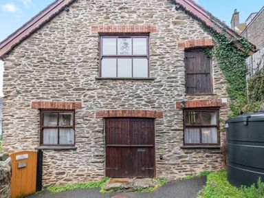 Stone building with wooden doors and windows with brick accents and ivy on the side at The Old Smithy in Lynton