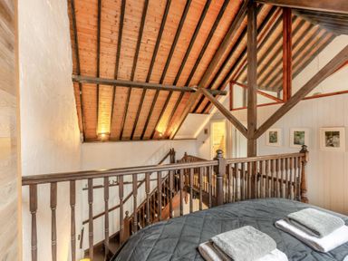 An attic bedroom with wooden beams a staircase and towels on a bed at The Old Smithy in Lynton