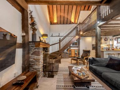 A living room with wooden beams stone fireplace and staircase a sofa and armchair at The Old Smithy in Lynton