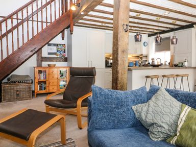 An open living space with a blue sofa and pillows a brown chair and footrest a wooden cabinet and a kitchen area with stools and pendant lights at The Old Smithy in Lynton